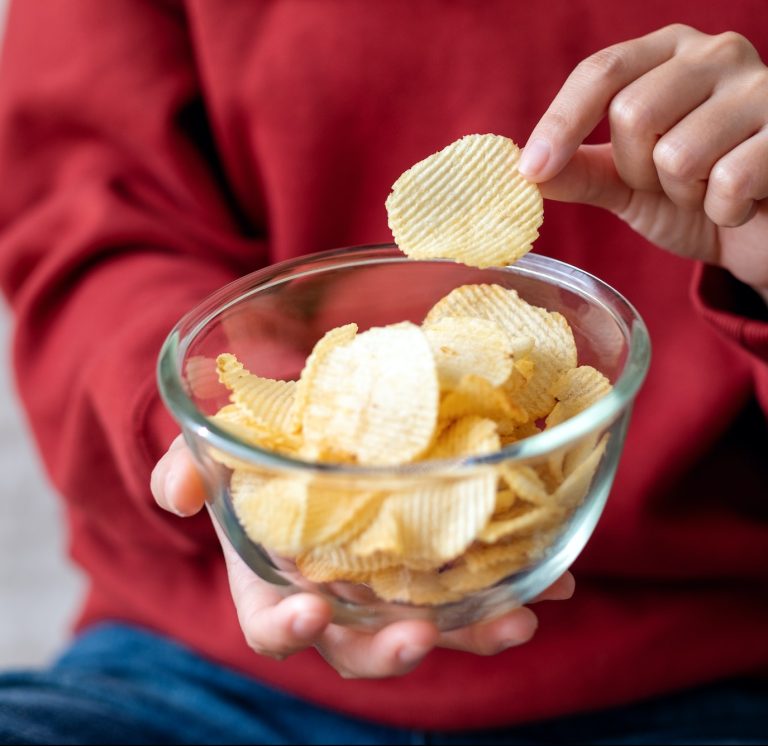 Closeup image of a woman picking and eating potato chips at home