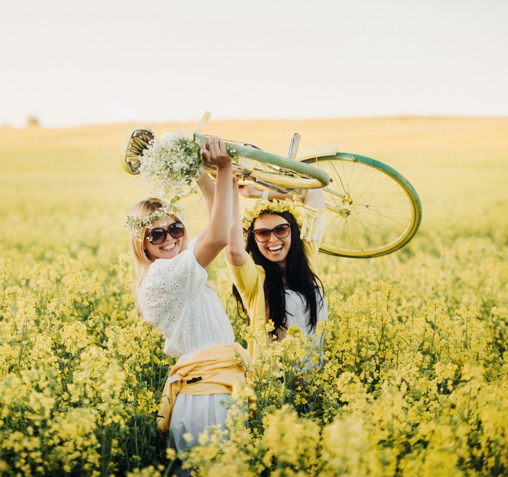 two women in a rapeseed field with a bicycle enjoy a walk in nature rejoicing